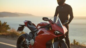 夕暮れ時の海岸沿いに美しく停車する赤いパニガーレと佇む日本人ライダー。魅力的なデザインの一方で「ドゥカティは燃える」という噂の真相や維持費について解説するブログ記事のアイキャッチ。