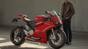 光が差し込むガレージで、赤いドゥカティを静かに見つめる50代の日本人男性。ドゥカティの中古が安い理由を理解し、賢い一台を選ぶシーンをイメージした写真。