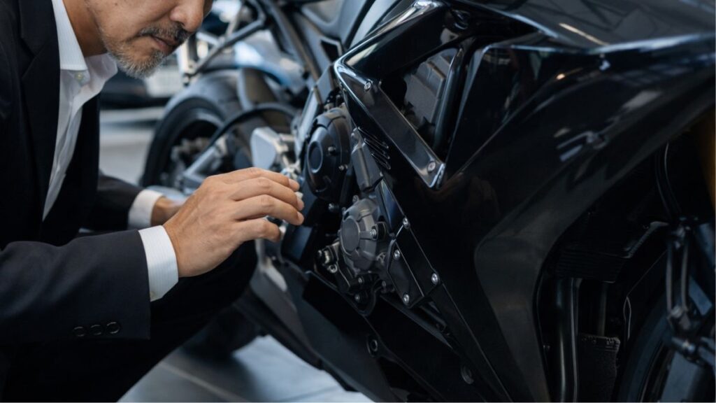 中古バイク店で車両の状態を確認する50代の男性。整備費用や金利を含めた総額を考慮し、バイクローンはやめたほうがいい失敗を避けるための慎重な観察を表現した画像です。