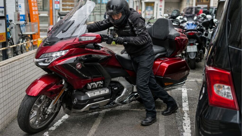 狭い駐輪場でホンダ・ゴールドウイングの取り回しに苦労する日本人男性ライダー