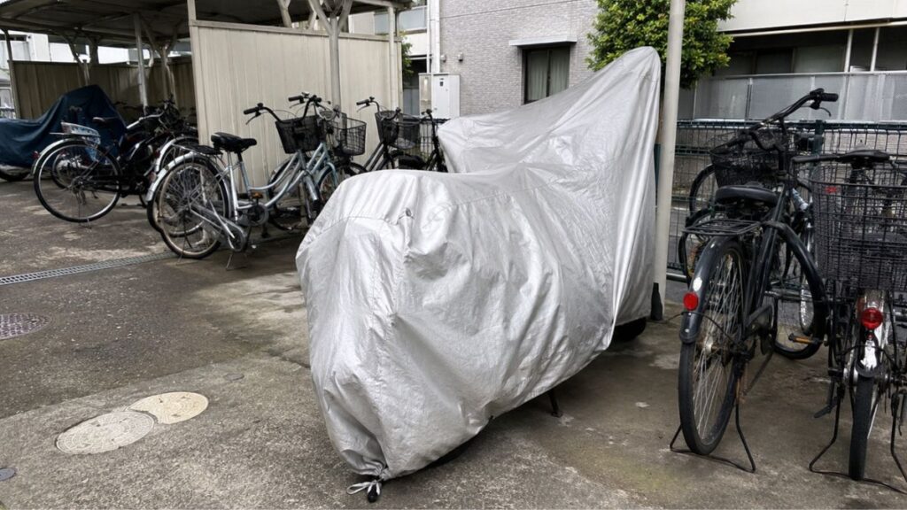 アパートの屋外共有駐輪場にカバーをかけて停められているバイク